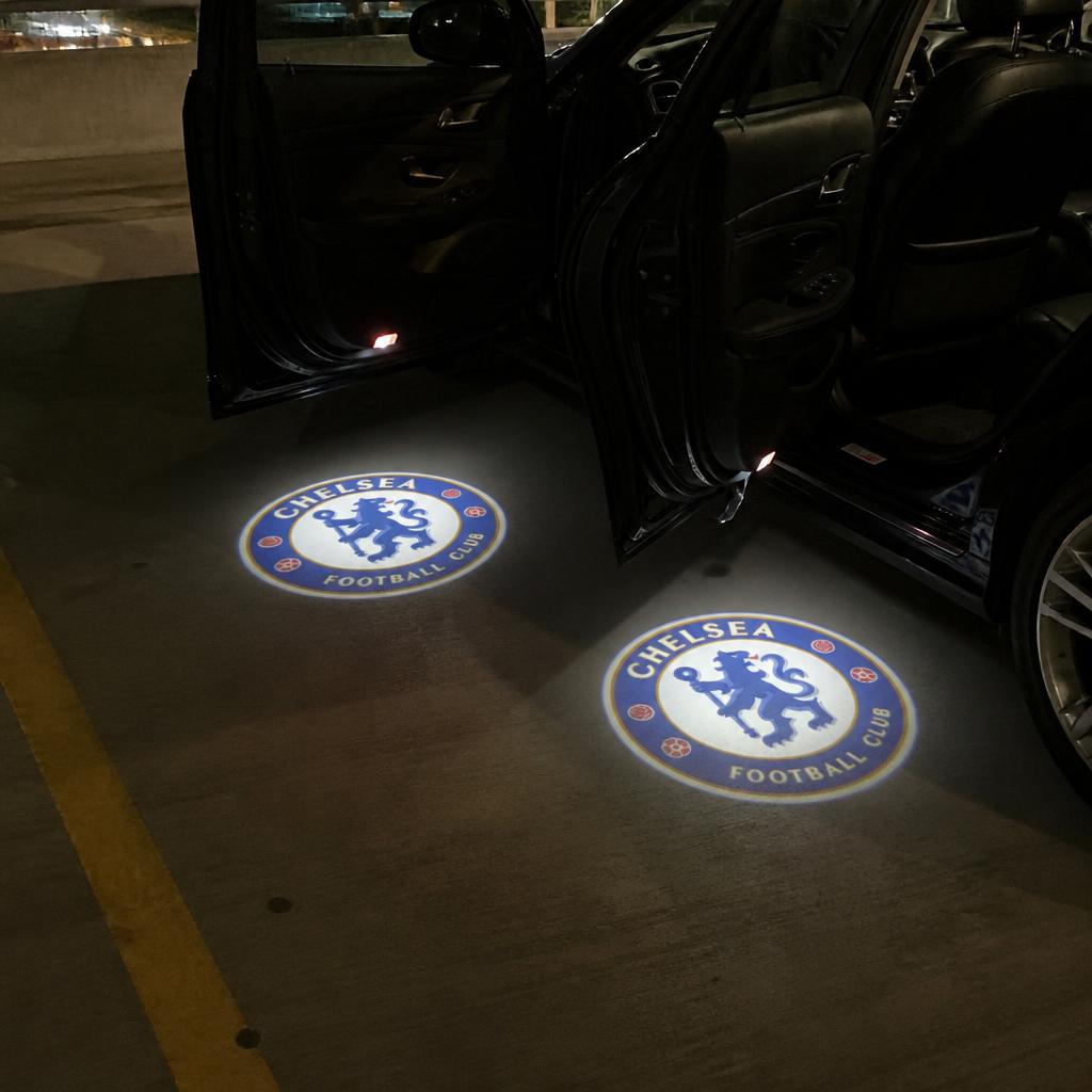 Two Chelsea crests projected onto a parking garage floor from both open car doors